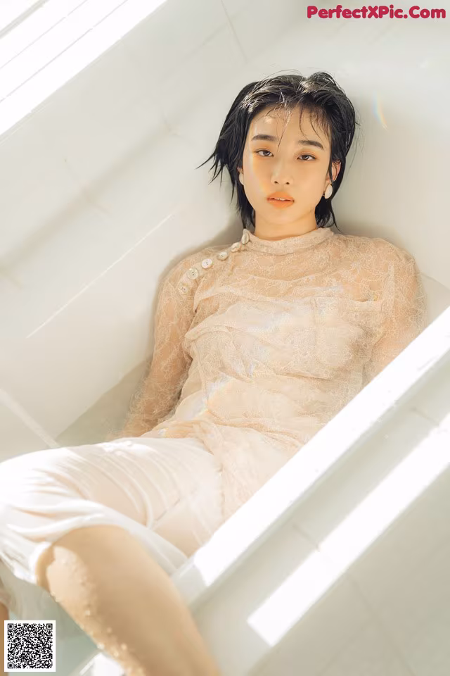 A woman sitting in a bathtub in a white dress.