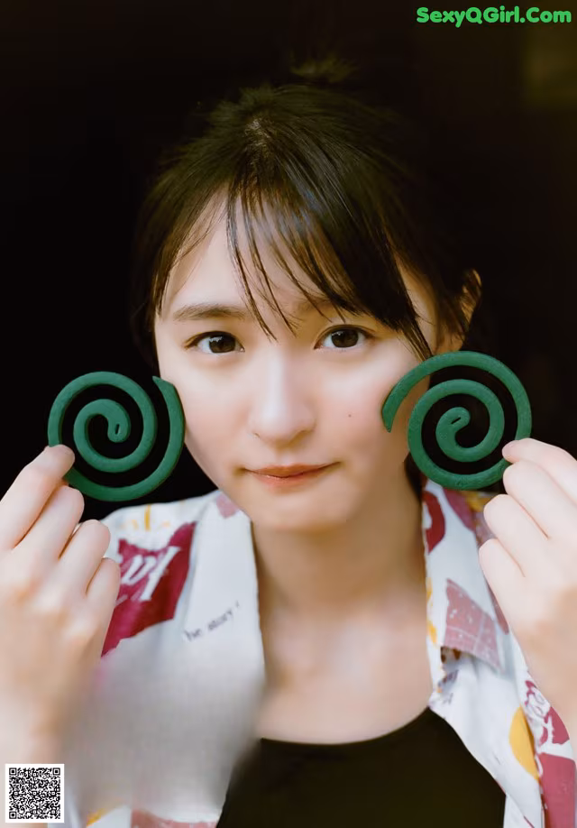 A woman holding two green spirals in front of her face.