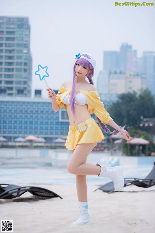 A woman in a yellow bikini holding a wand on a beach.