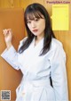 A woman in a white kimono leaning against a wooden wall.