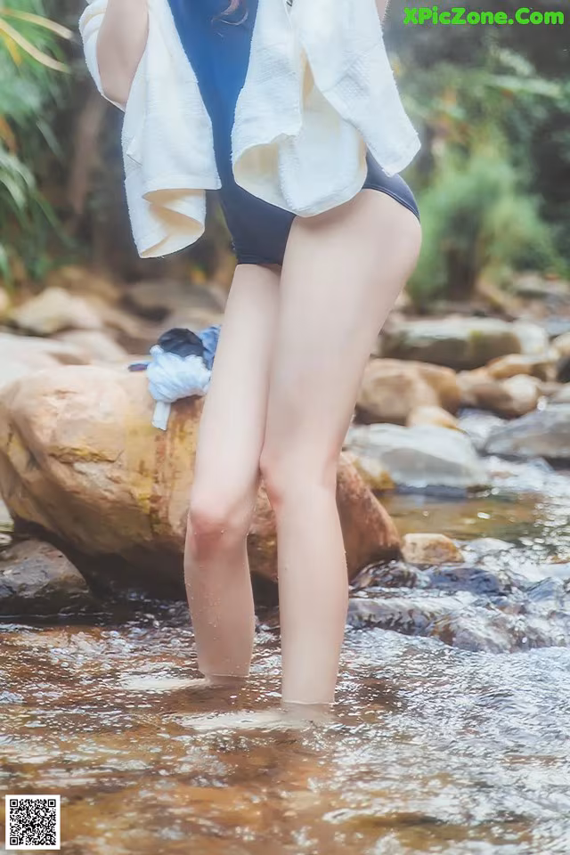 A woman standing in a stream with a towel on her head.