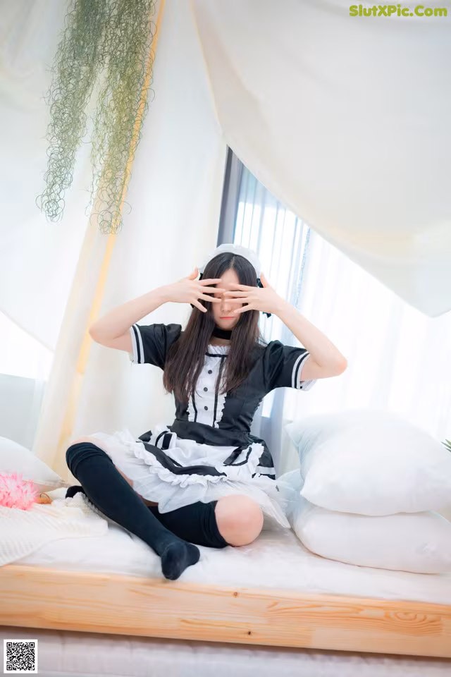 A woman sitting on a bed with her hands covering her eyes.