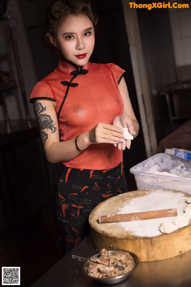 A woman in a red cheongsam preparing food in a kitchen.