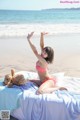 A woman in a red and white bikini sitting on a bed with a teddy bear.