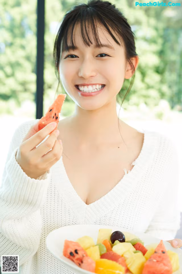 A woman holding a plate of fruit and a slice of watermelon.