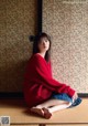 A woman in a red sweater sitting on the floor.