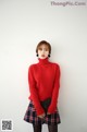 a woman in a red sweater and plaid skirt posing for a picture