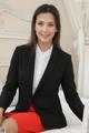 A woman in a black blazer and red skirt sitting on a bed.