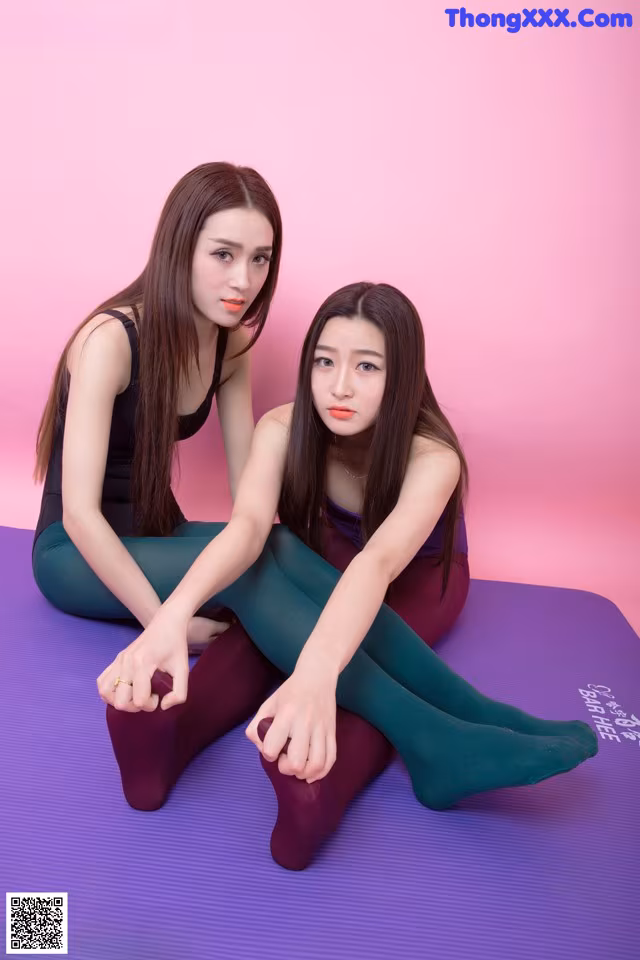 Two young women sitting on a purple yoga mat.