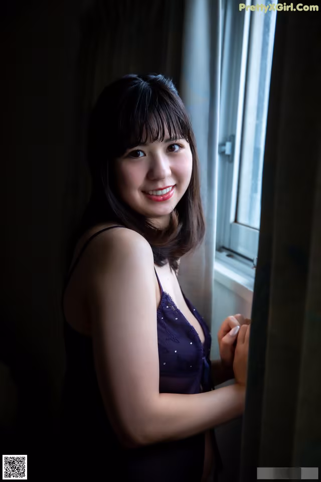 A woman in a purple dress standing by a window.