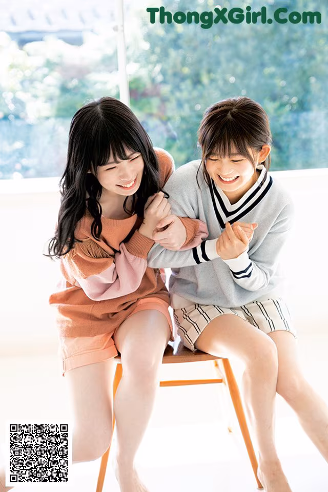 Two young women sitting on a chair smiling at each other.