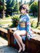 A woman in a blue kimono sitting on a wooden bench.