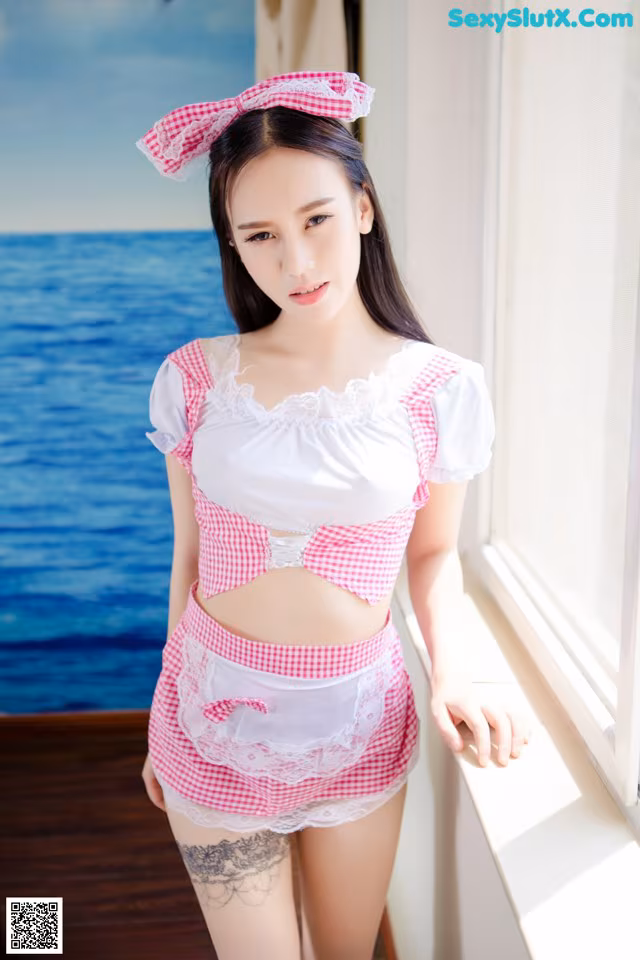 A woman in a pink and white dress standing by a window.