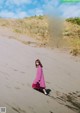 A woman in a pink dress walking on a sandy beach.