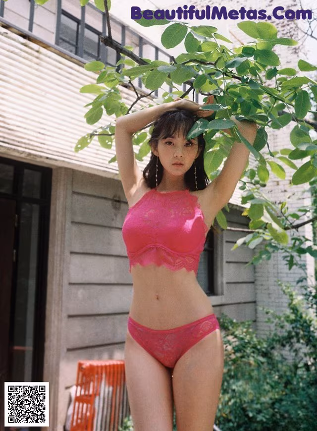 A woman in a pink lingerie standing next to a tree.